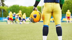 Back view of a football player holding a yellow helmet on his left hand