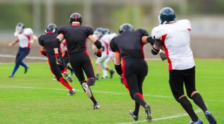 Back view of 4 football players running on a line