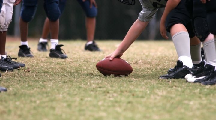 A youth football player bending down to hold the ball against the grass, getting ready to start the game