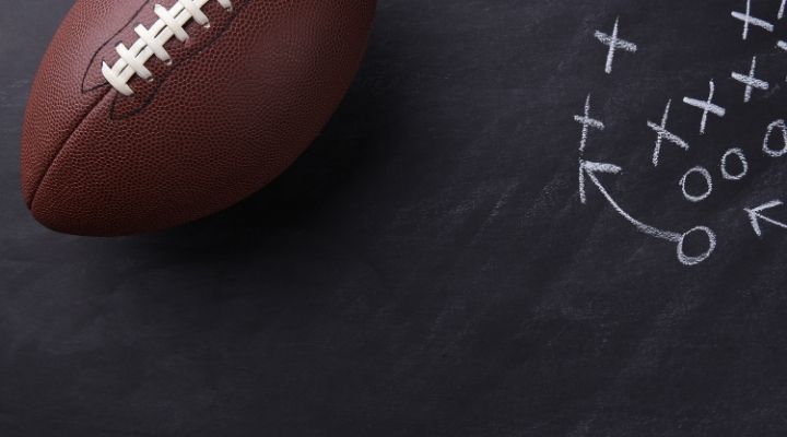 Top view of a football laying on top of a blackboard with a diagram of a play written on it in chalk
